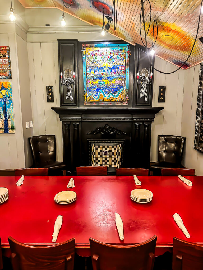 A long red table set with plates and napkins in the Napoleon Room at Tibby’s Brandon, facing a black fireplace below a colourful folk-art painting